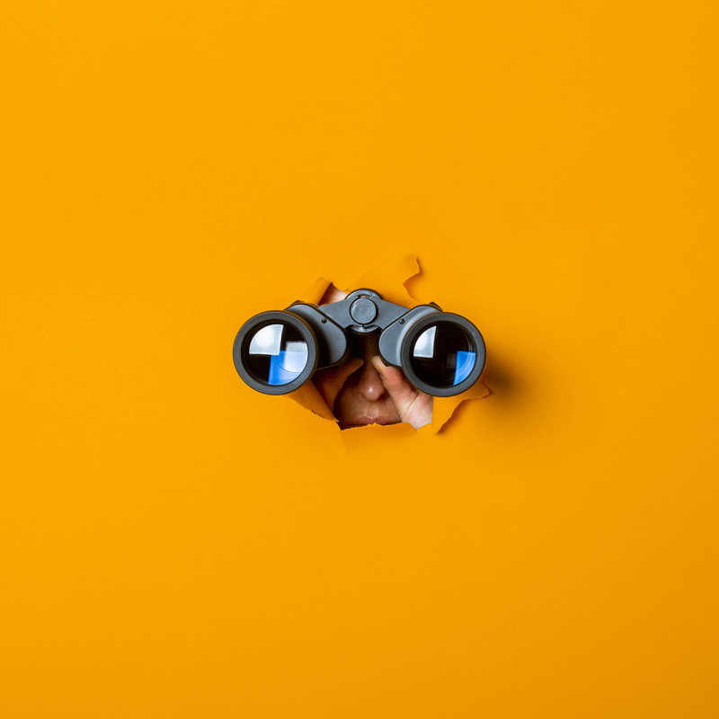 Person schaut durch ein Fernglas auf orangefarbener Fläche – Symbol für die Suche nach Personal und Karrierechancen bei Breitband Ortenau